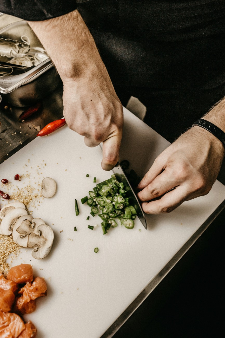 Hands slicing chillies on the board, mise en place around them